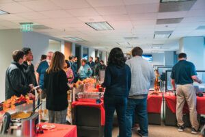 A group of coworkers gathered around a table laden with Thanksgiving dishes, including roast turkey, mashed potatoes, and gravy.